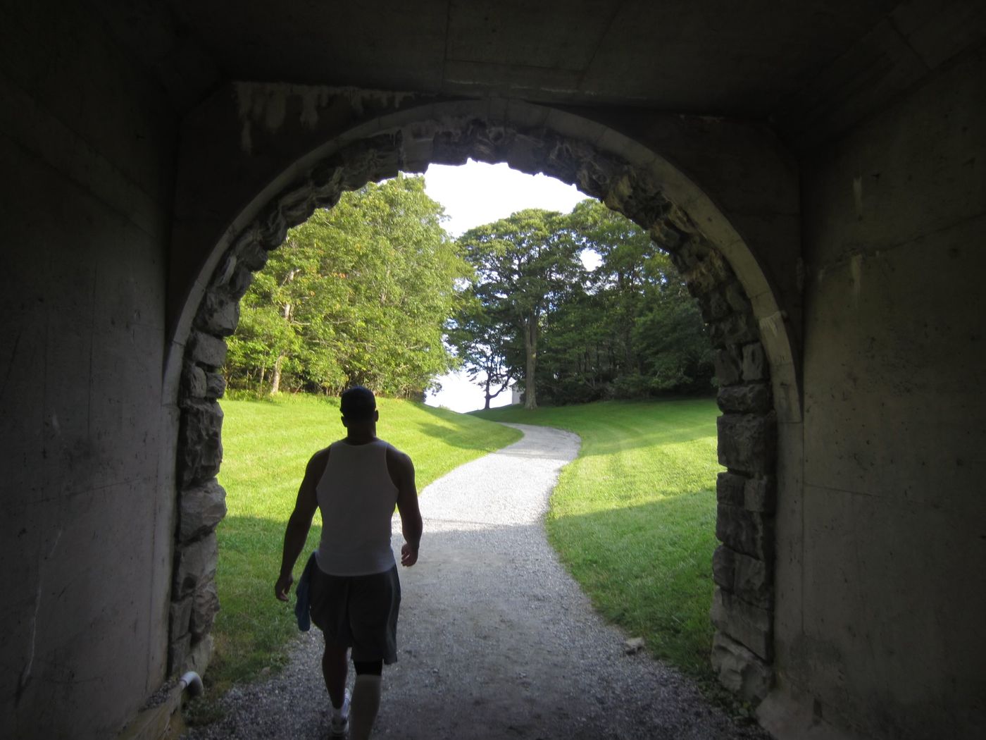 Pryce walking through a stone archway toward a green field